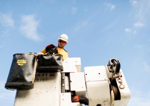 Lineworker looking down from a bucket against a blue sky